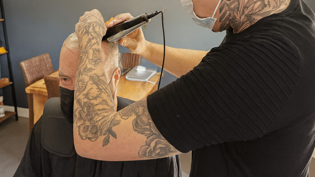 A stylist is shaving an old guy's head for hair system attachment