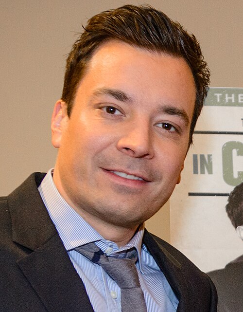 Man with short styled dark hair wearing a black suit and gray tie, smiling at an indoor event