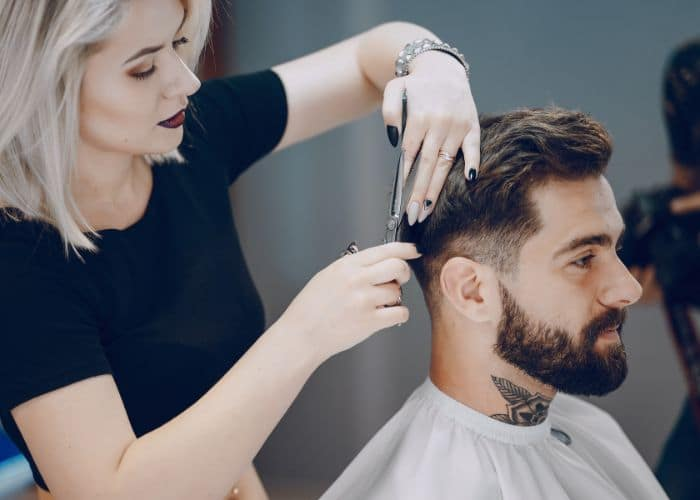 A female stylist is making a haircut for a man