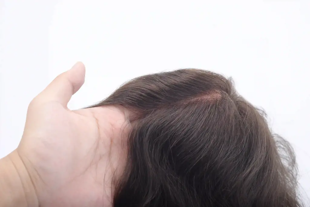 A hand holding a lace hair system with brown hair